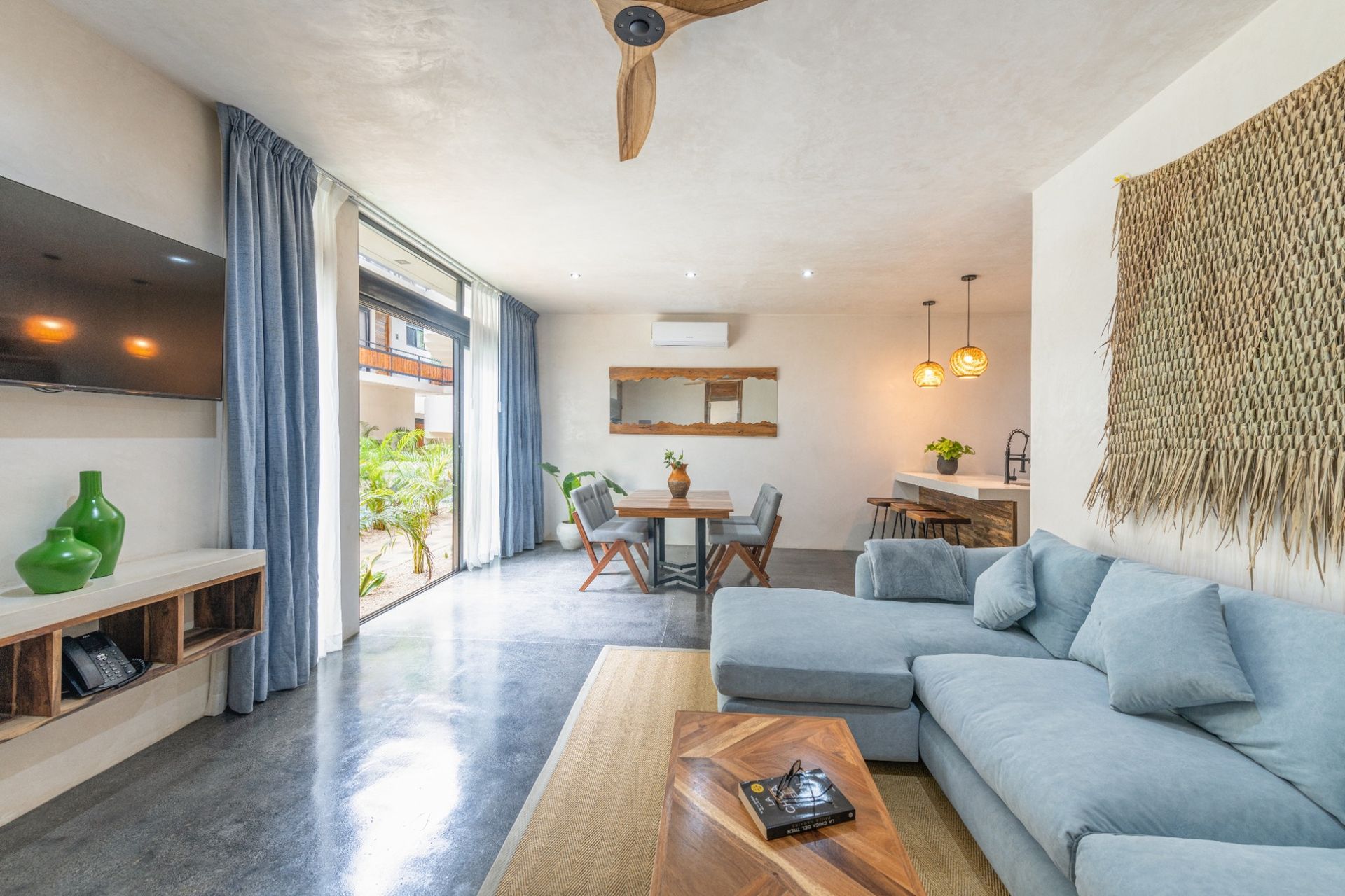 Modern living room with blue sectional, open to a patio, dining area, and concrete floor.