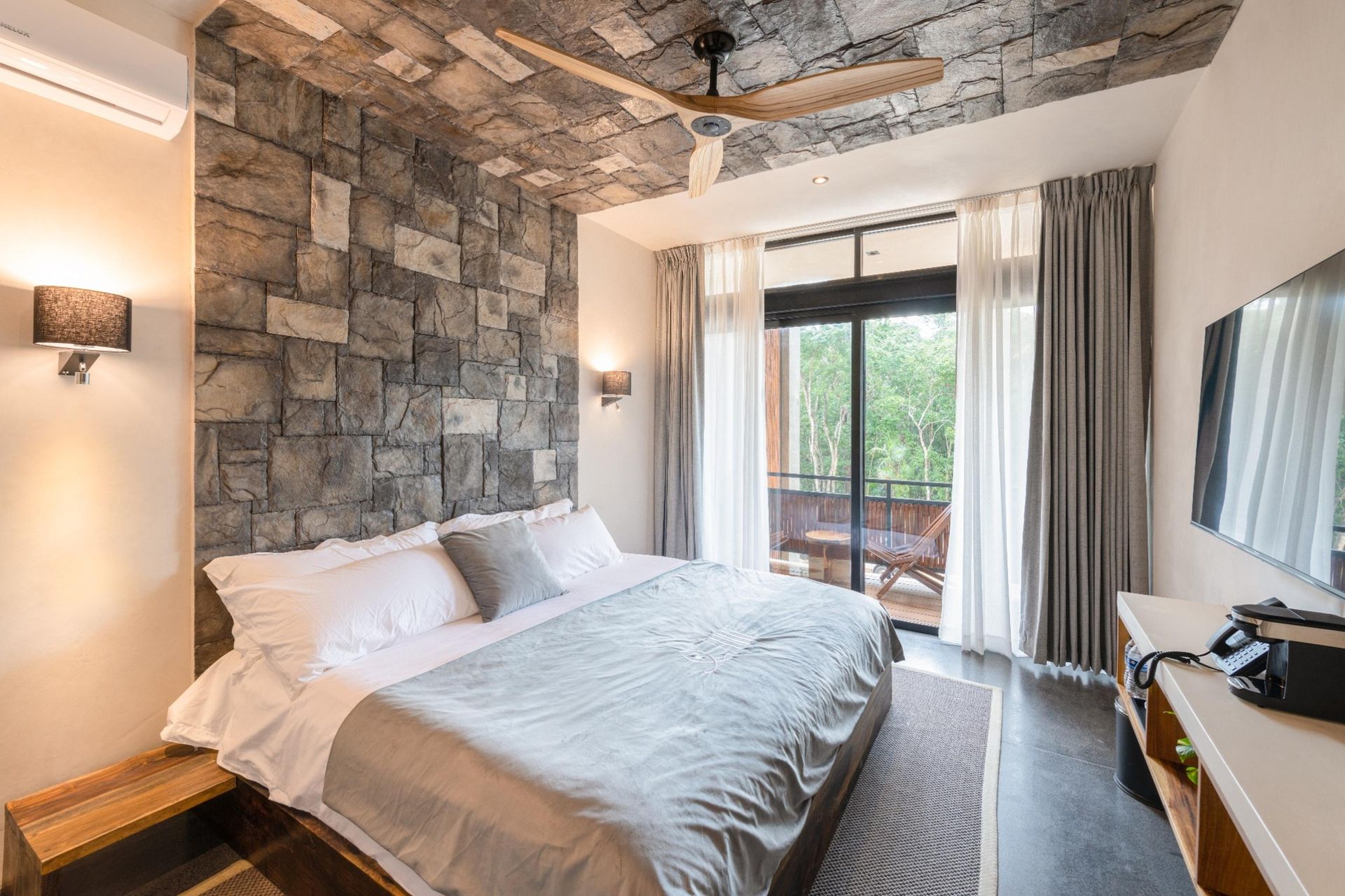 Modern bedroom with stone accent wall, king bed, and sliding doors to a balcony.
