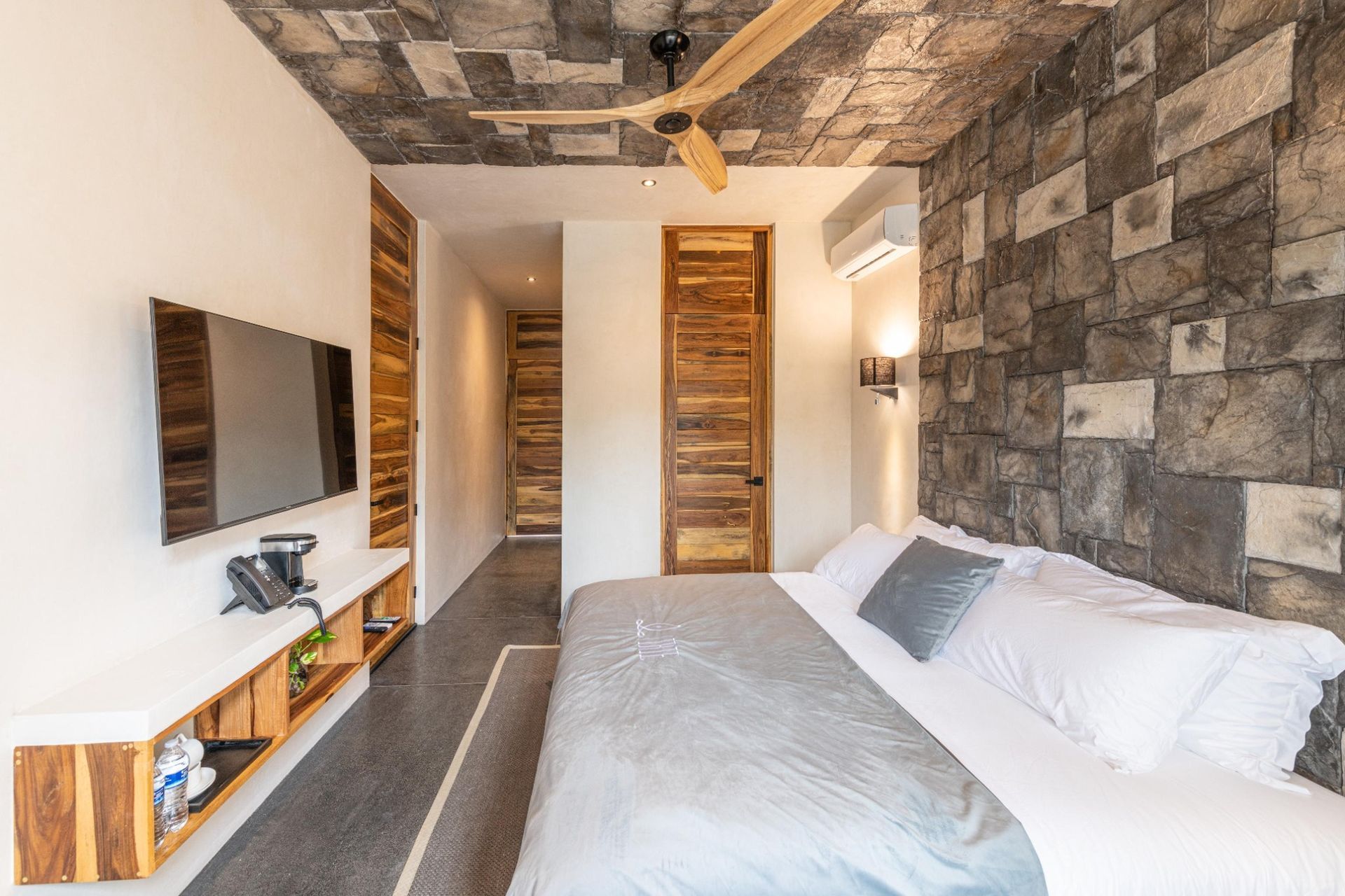 Modern bedroom with stone accent wall, white bedding, wall-mounted TV, and wooden doors