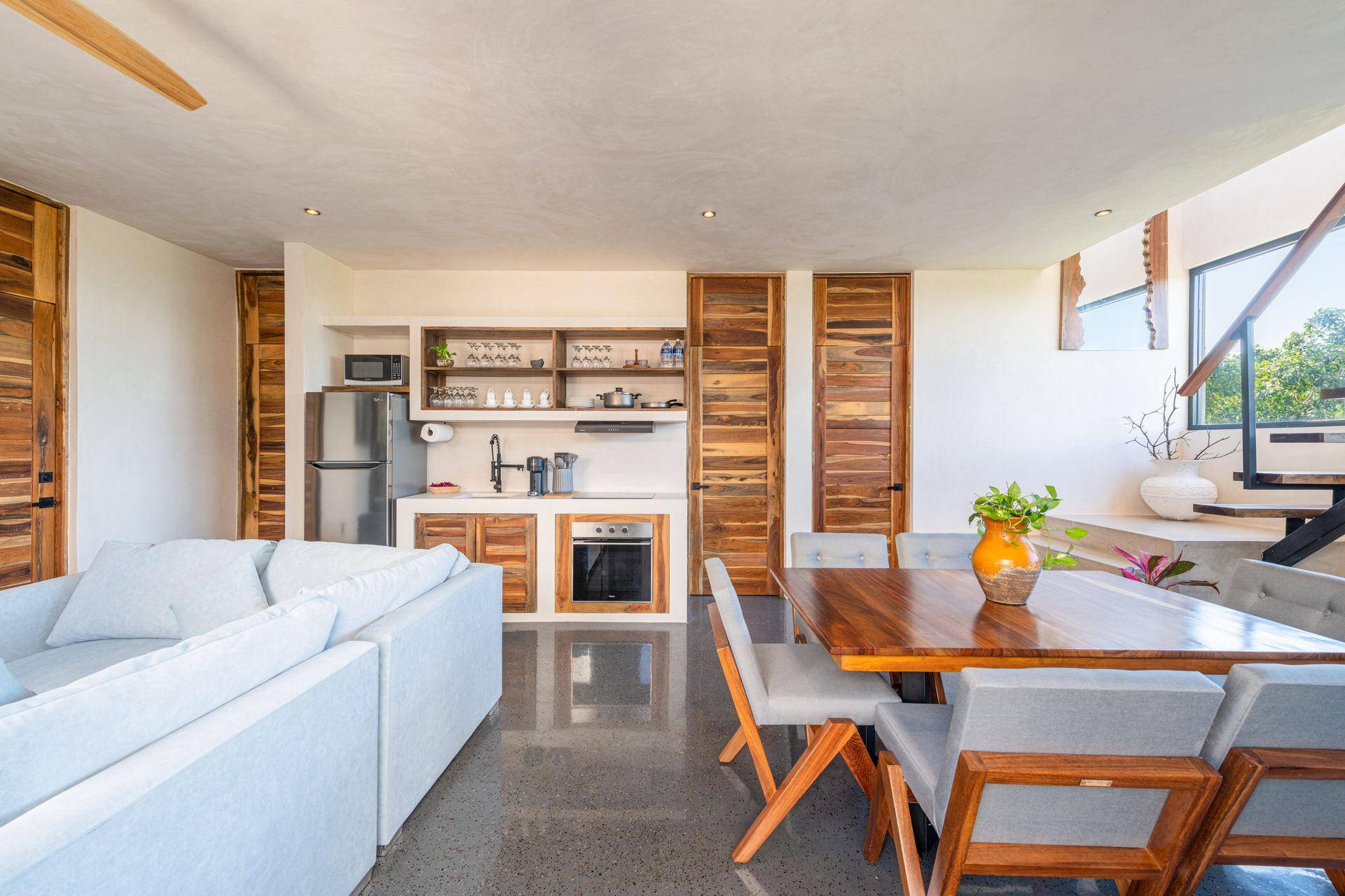 Bright modern living and dining area with white sofa, wooden table, shelves, and ocean view window