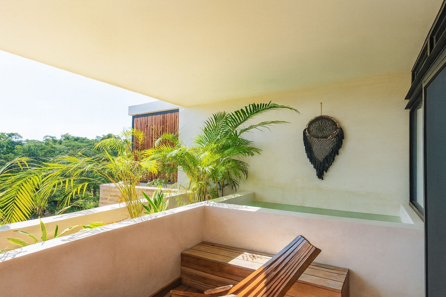 Balcony with wooden chair, potted plants, and ocean view in bright sunlight