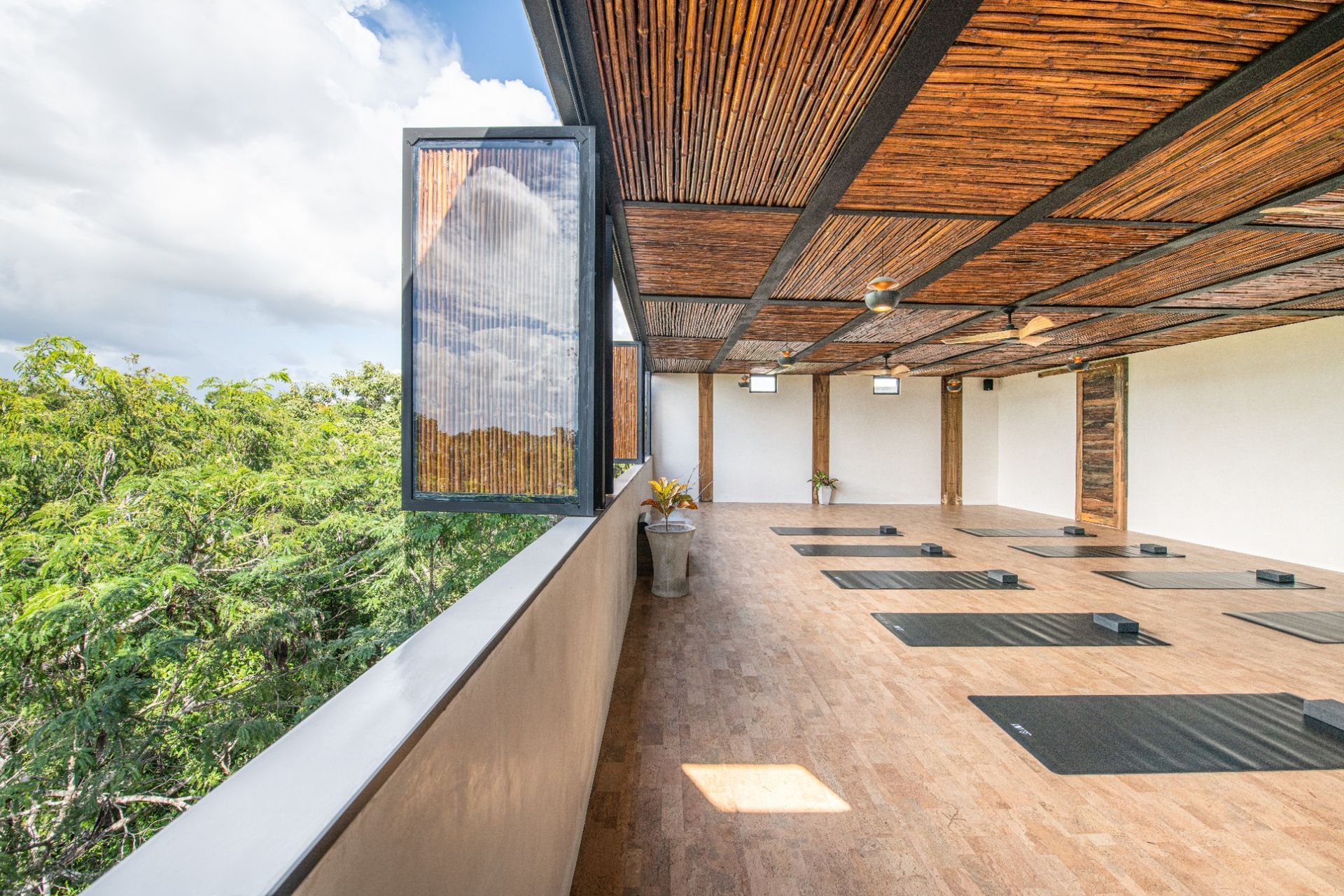 Open-air balcony with wooden ceiling, yoga mats, and a view of green trees and blue sky
