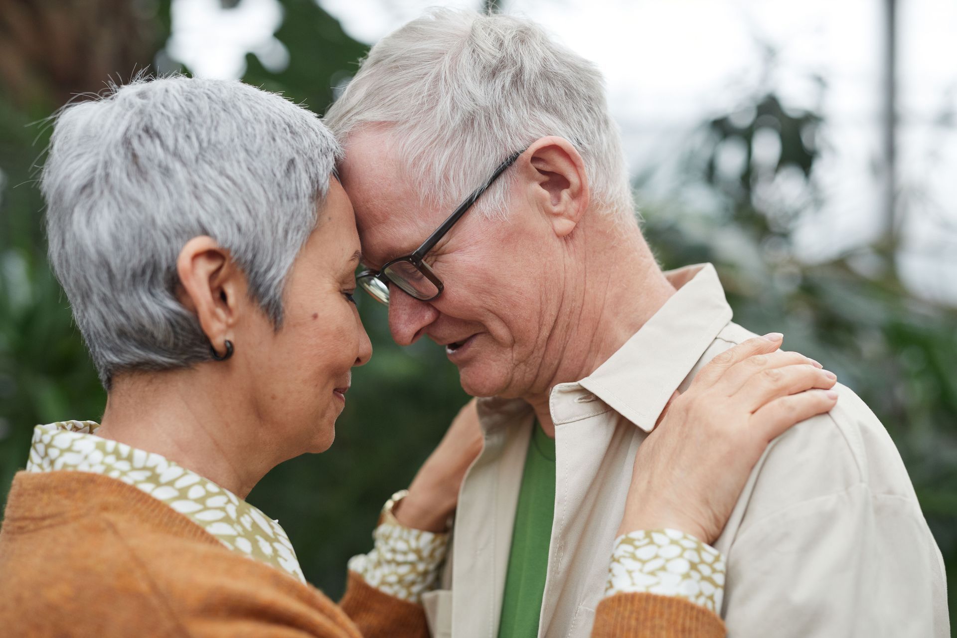 Two smiling people touching foreheads outdoors, sharing an intimate moment.