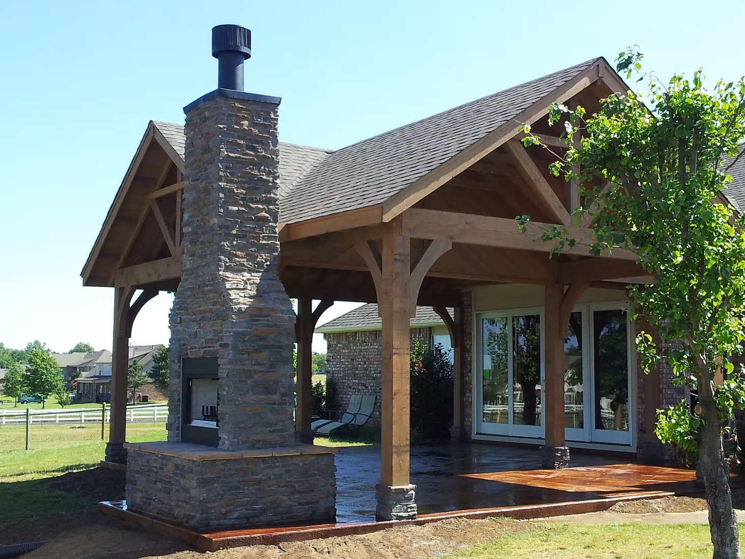 Small stone-and-wood pavilion with a pitched roof and chimney in a grassy outdoor setting
