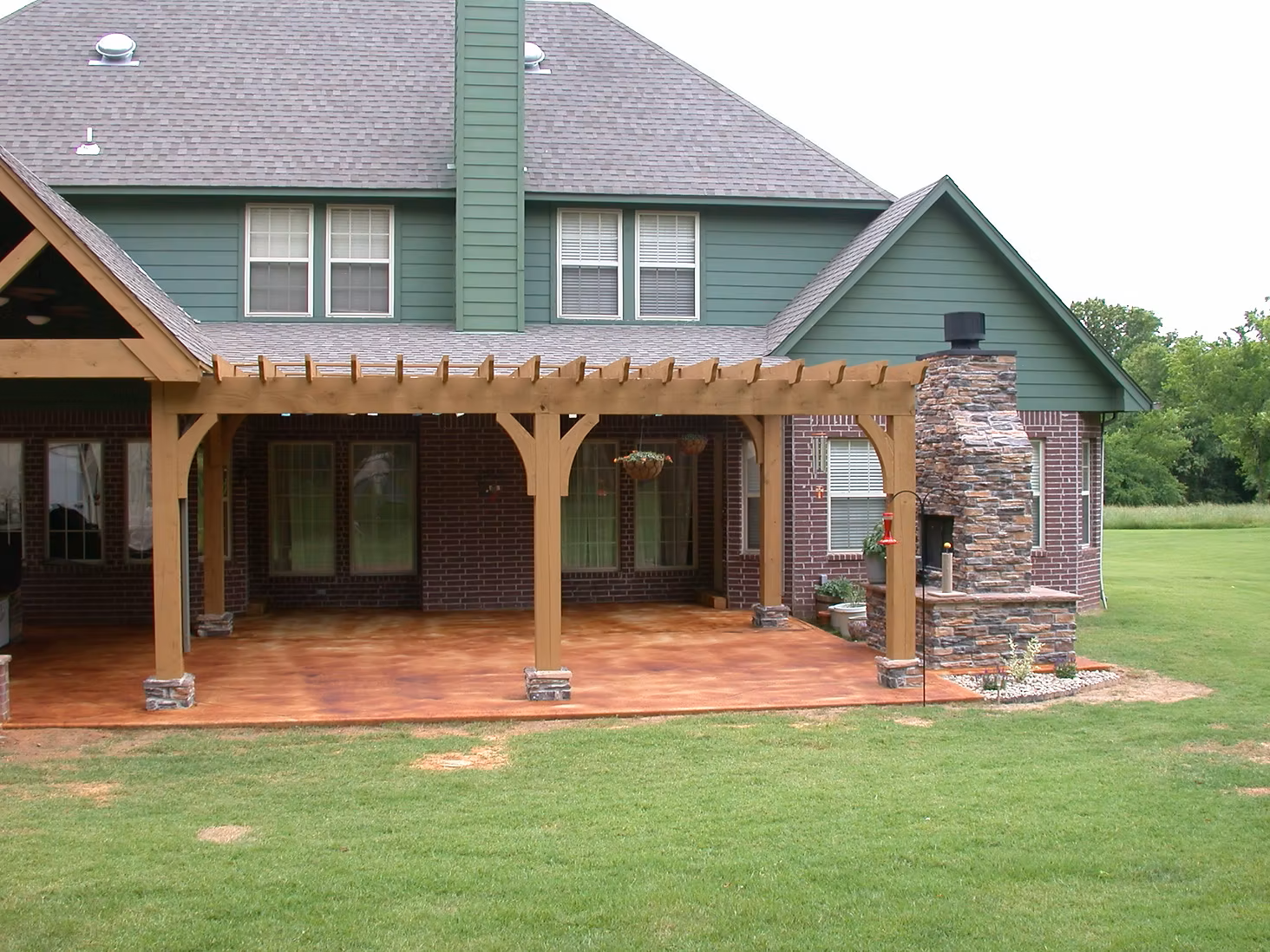 Back patio with wooden pergola, brick columns, and stone chimney on a green lawn