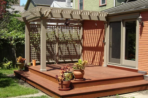 Backyard wooden deck with steps, pergola, and patio chairs against a house exterior