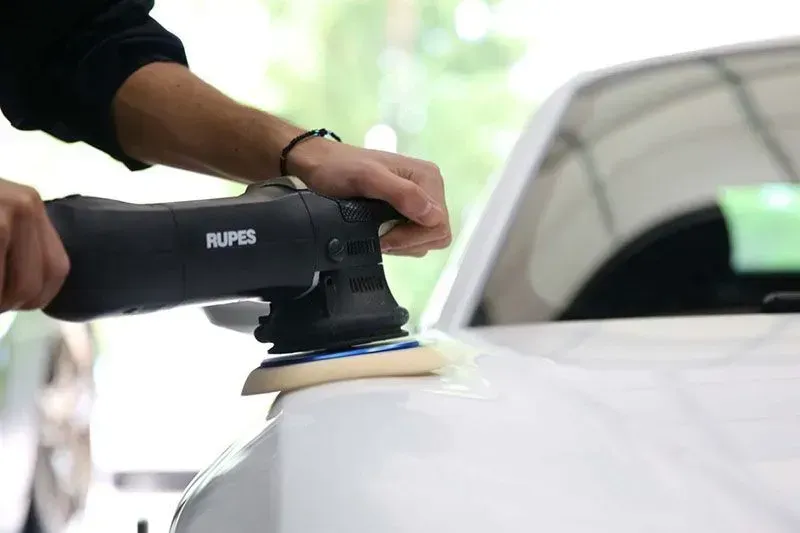 Paint Correction - A person is polishing a white car with a buffing machine.