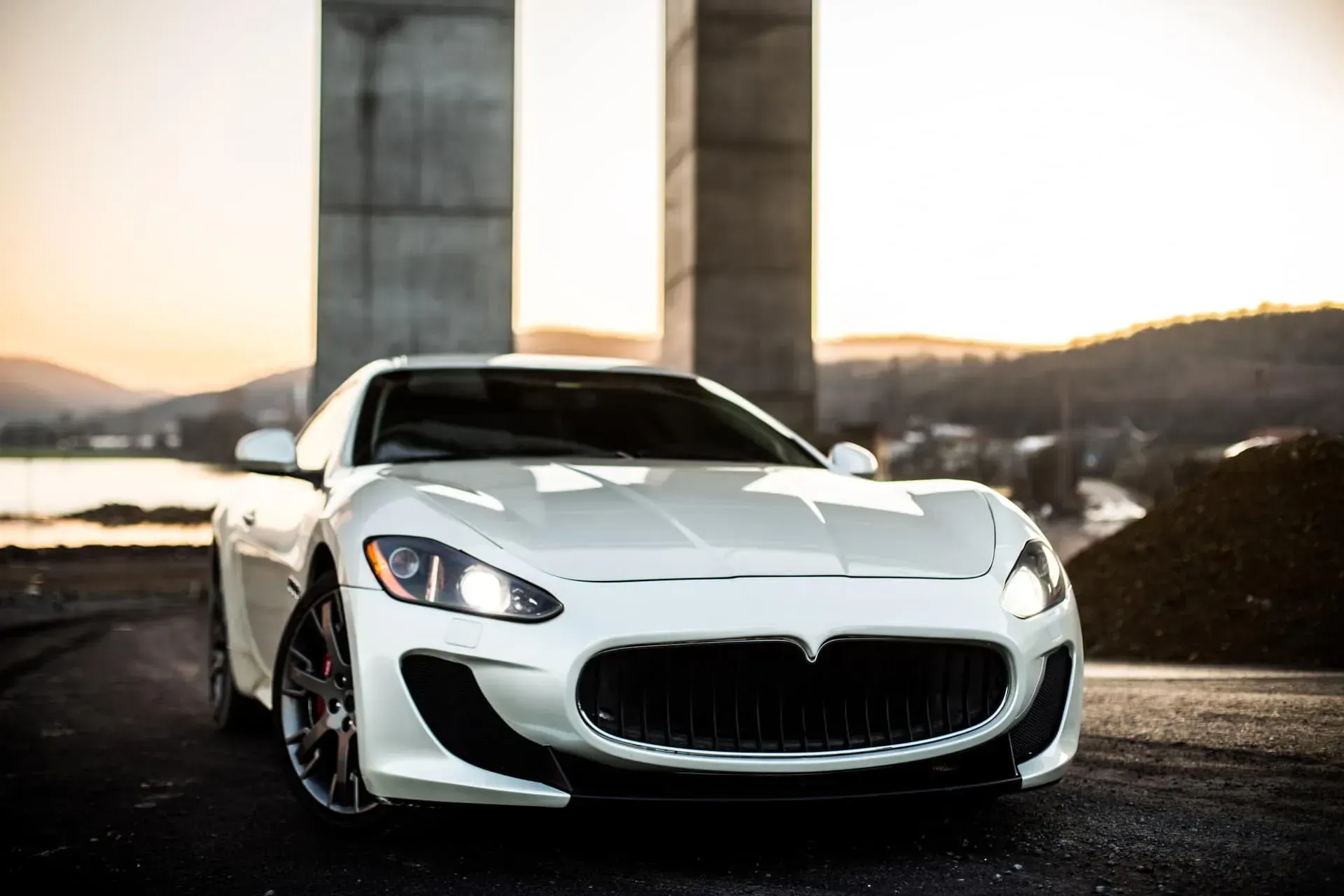 A white maserati granturismo is parked in front of a bridge .