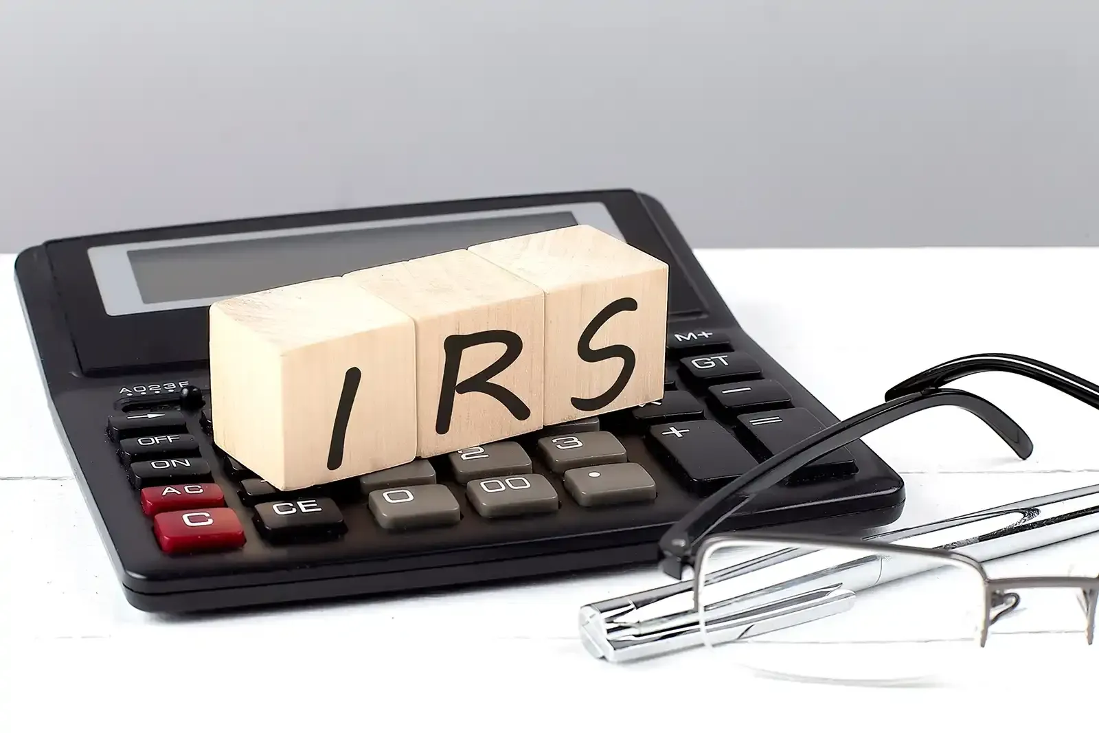 A calculator with a wooden block that says IRS on it, representing IRS debt.