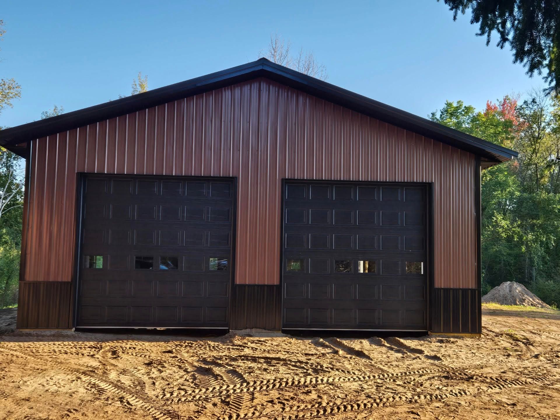 Brown metal garage with two black doors on a dirt lot under a blue sky