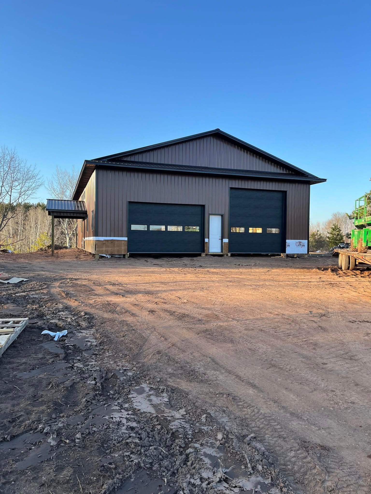 Brown metal workshop with two garage doors on a dirt lot under a clear blue sky