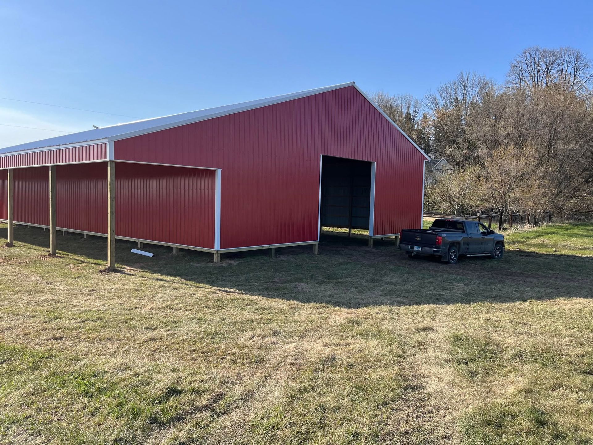 Red barn with open doorway beside a parked car in a grassy field under a clear sky
