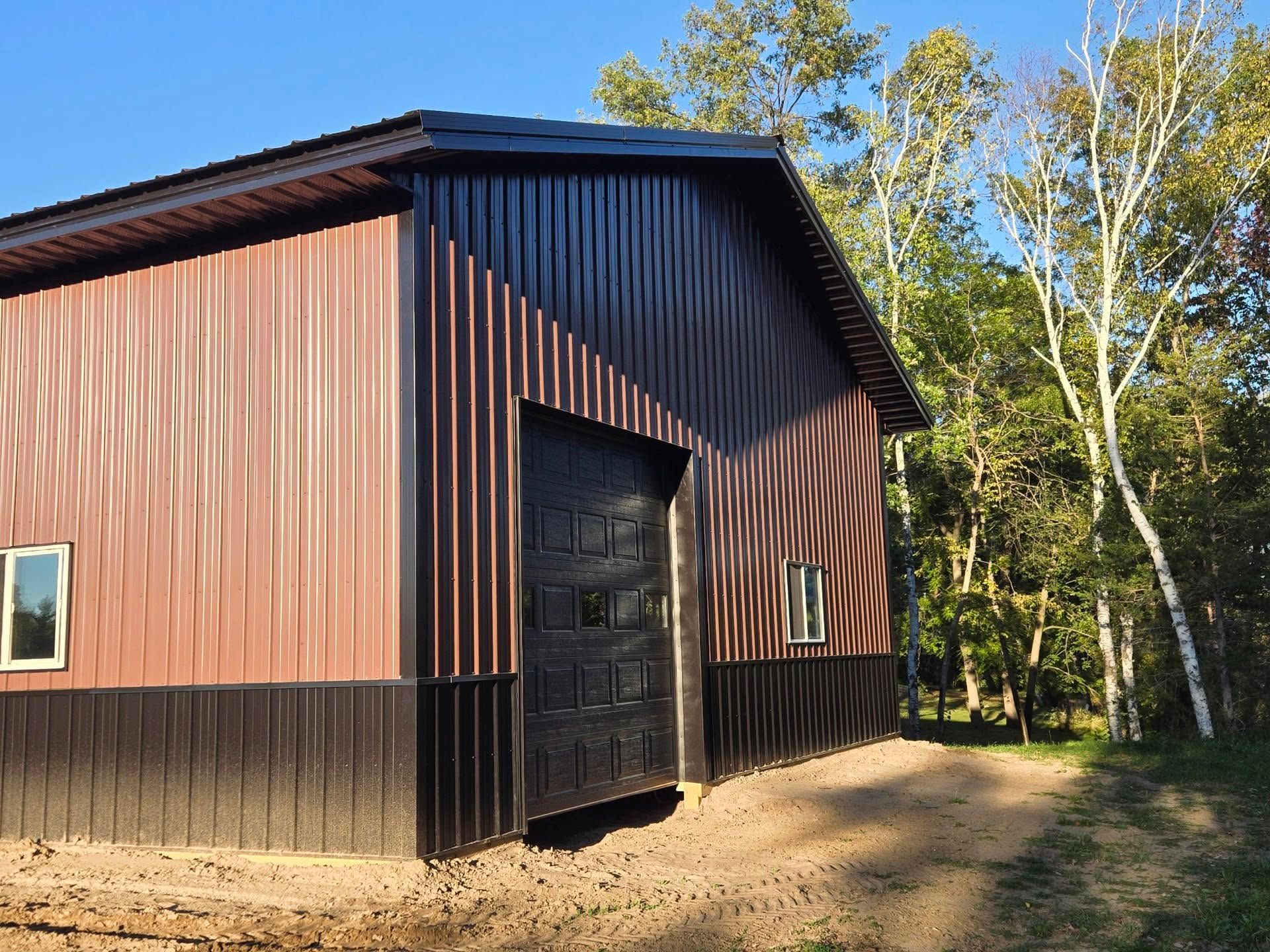 Red barn-style building with black trim and a large doorway beside a wooded dirt path.