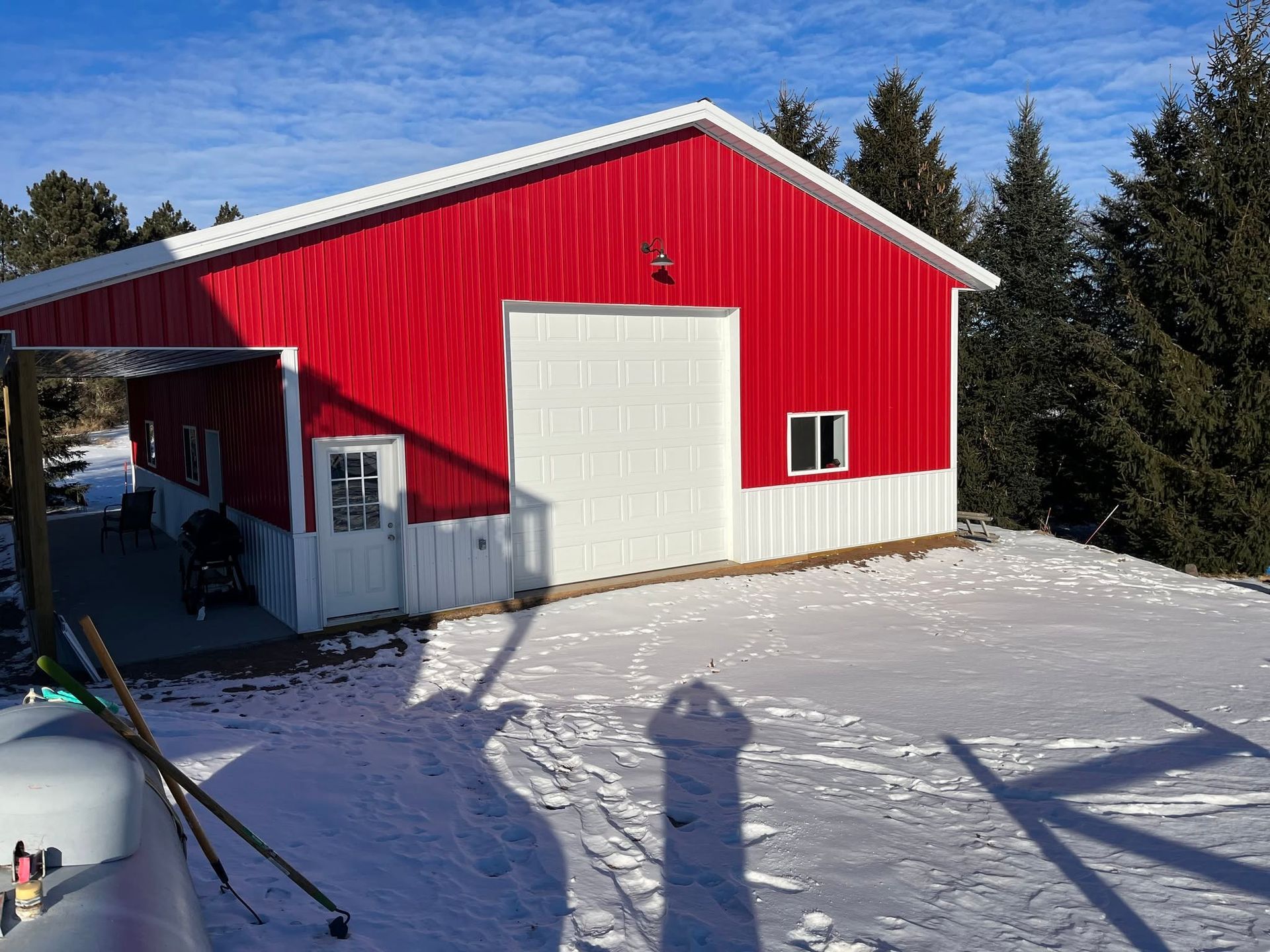 Red barn with white doors on a snowy hillside under a blue sky, with trees in the background