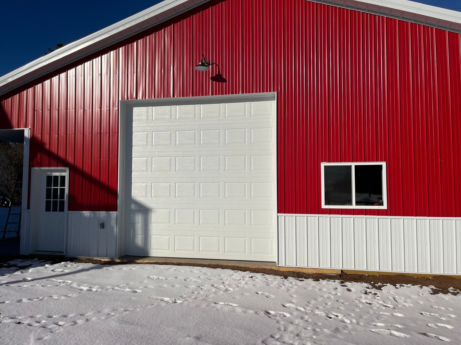 Red metal building with a large white garage door and snow-covered ground