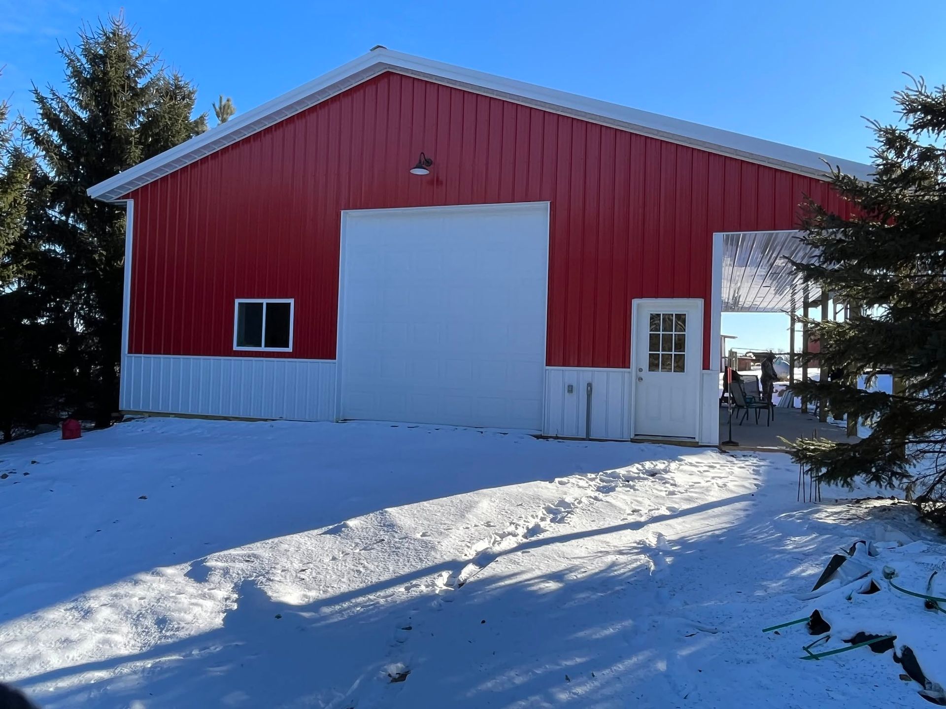 Red barn with a large white door in a snowy yard, viewed on a bright winter day