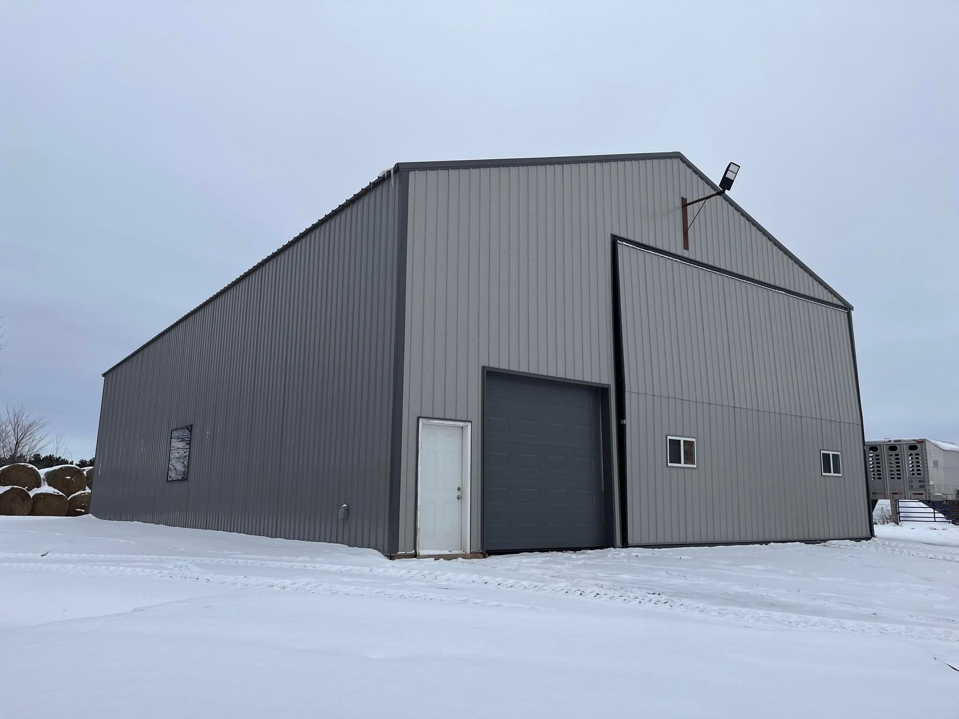 Gray metal warehouse in a snowy field under an overcast sky