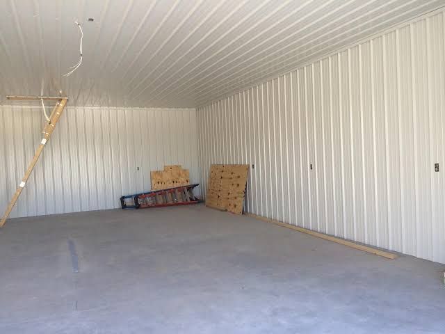 Empty garage with white paneled walls, gray concrete floor, and a ladder leaning on the left wall.