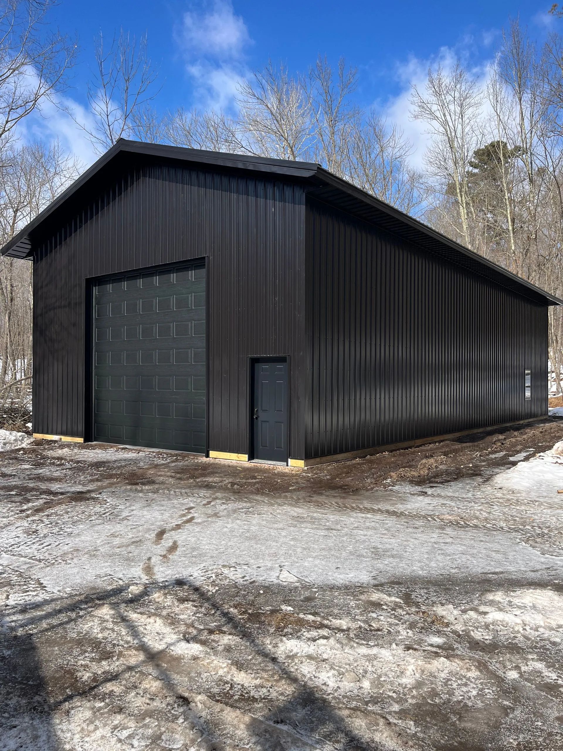 Yellow metal garage with white roll-up door and side door on a gravel lot, trees in the background
