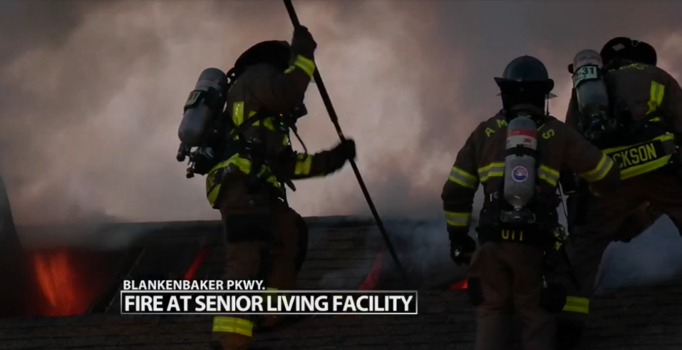 Firefighters in dark gear battle a blaze at a senior living facility at night.