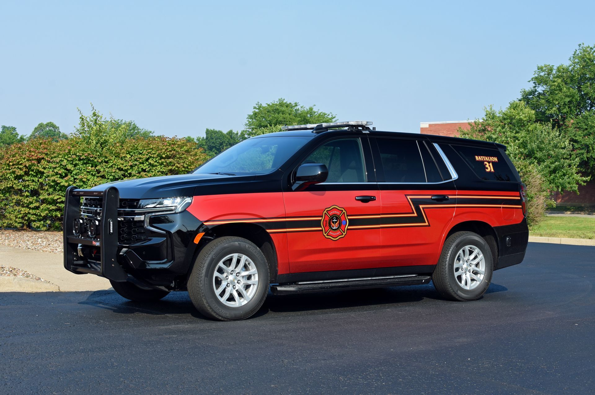 Red and black SUV with emergency vehicle markings, parked outdoors on a sunny day.