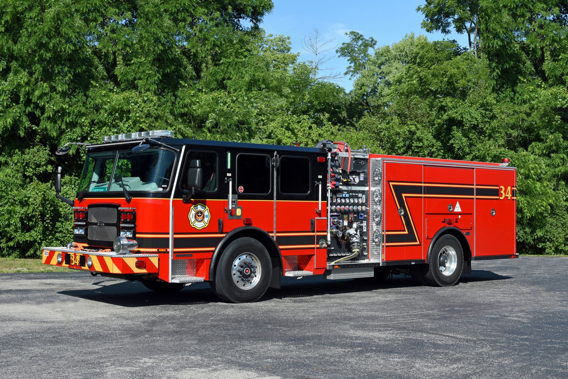 Red fire truck parked, black roof, emergency lights, silver equipment, green trees in the background.