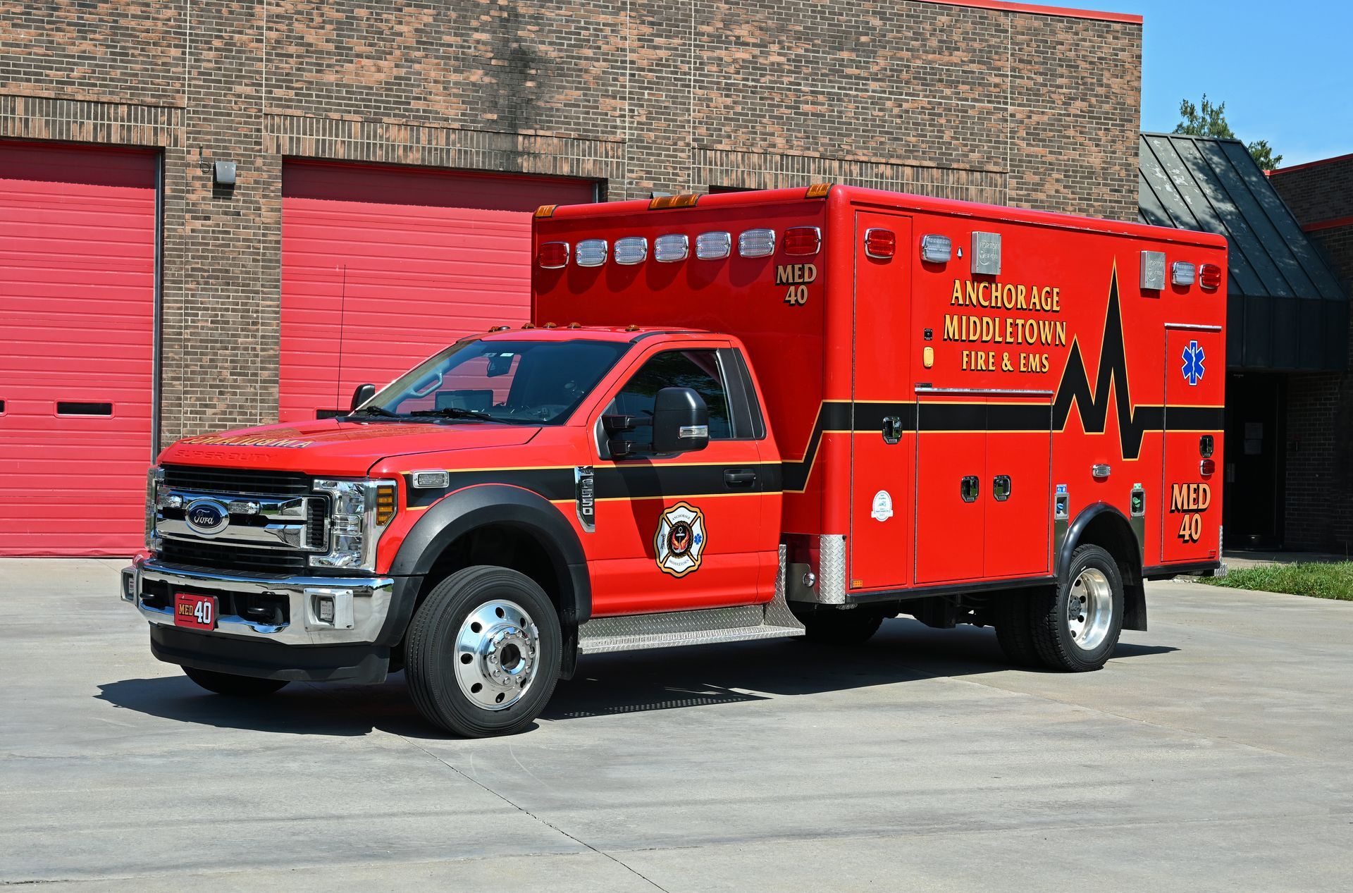 Red ambulance truck parked in front of a brick building. 