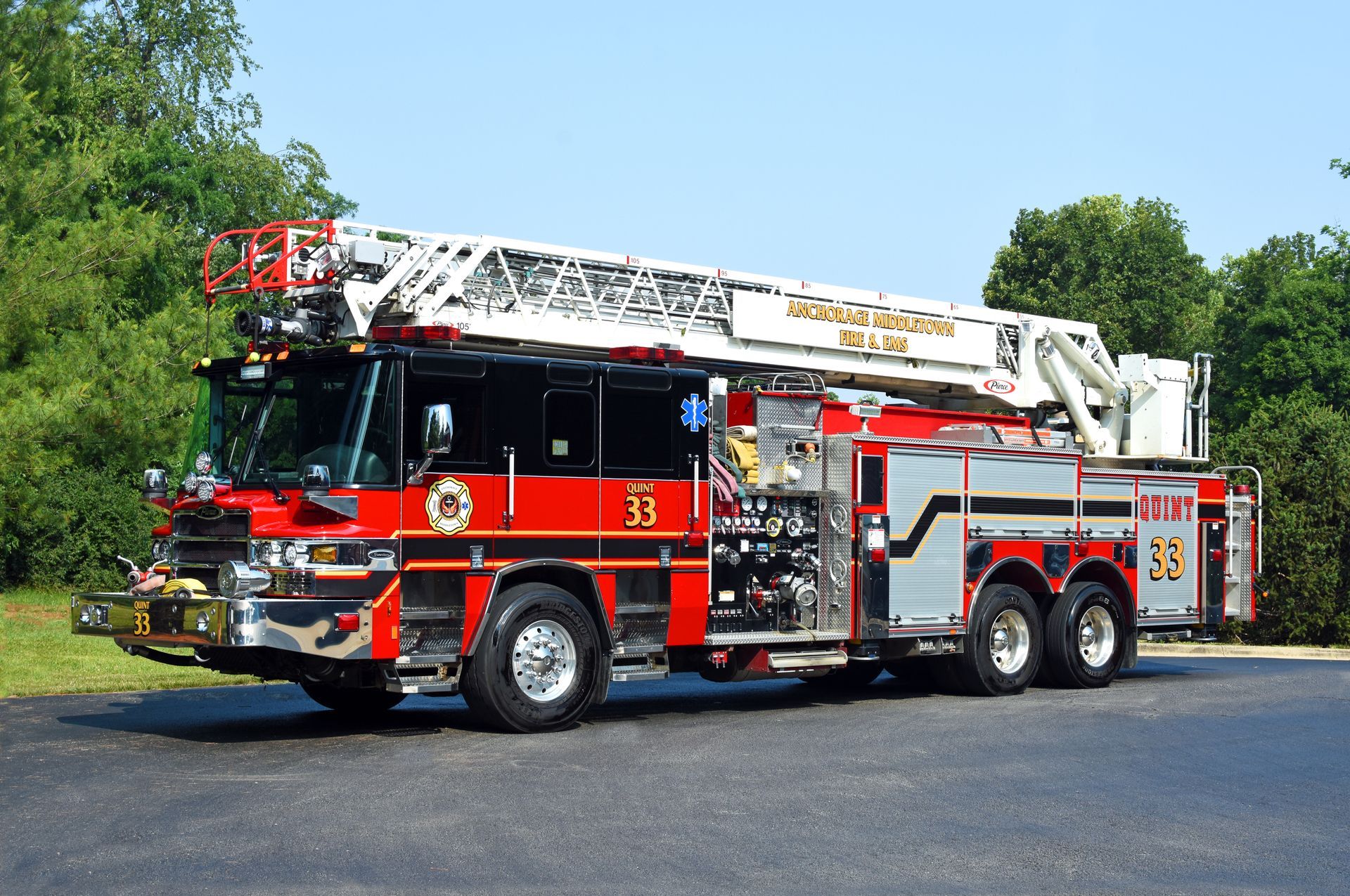 Red fire truck with extended ladder on a paved area, green trees in background.