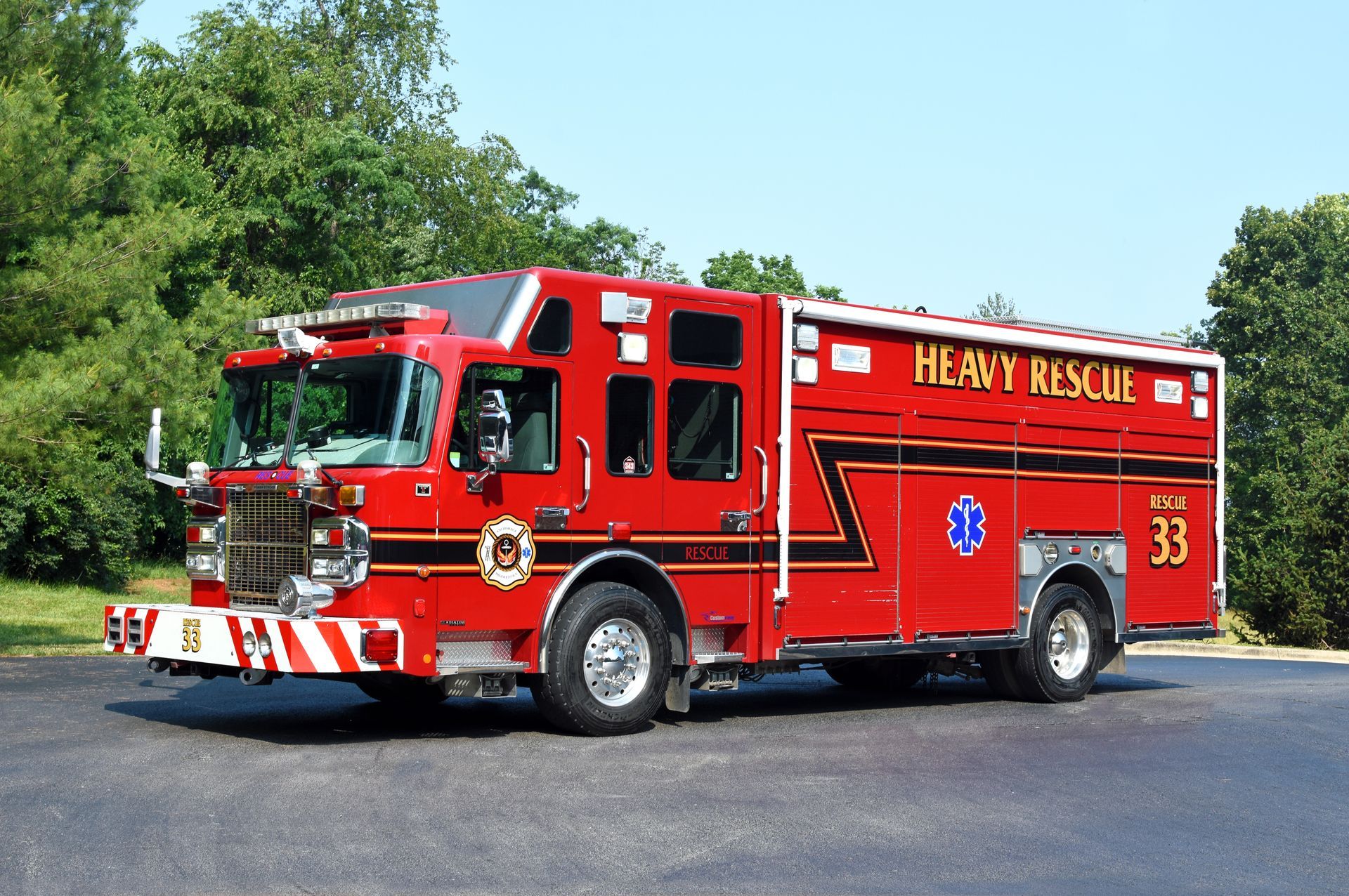 Red heavy rescue fire truck parked on pavement beside trees under a clear blue sky