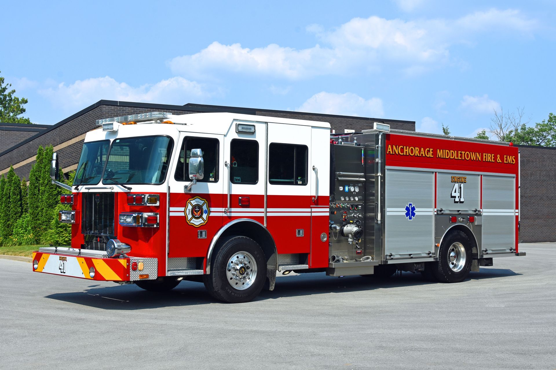 Red and white fire truck parked outdoors; building and blue sky in background. 