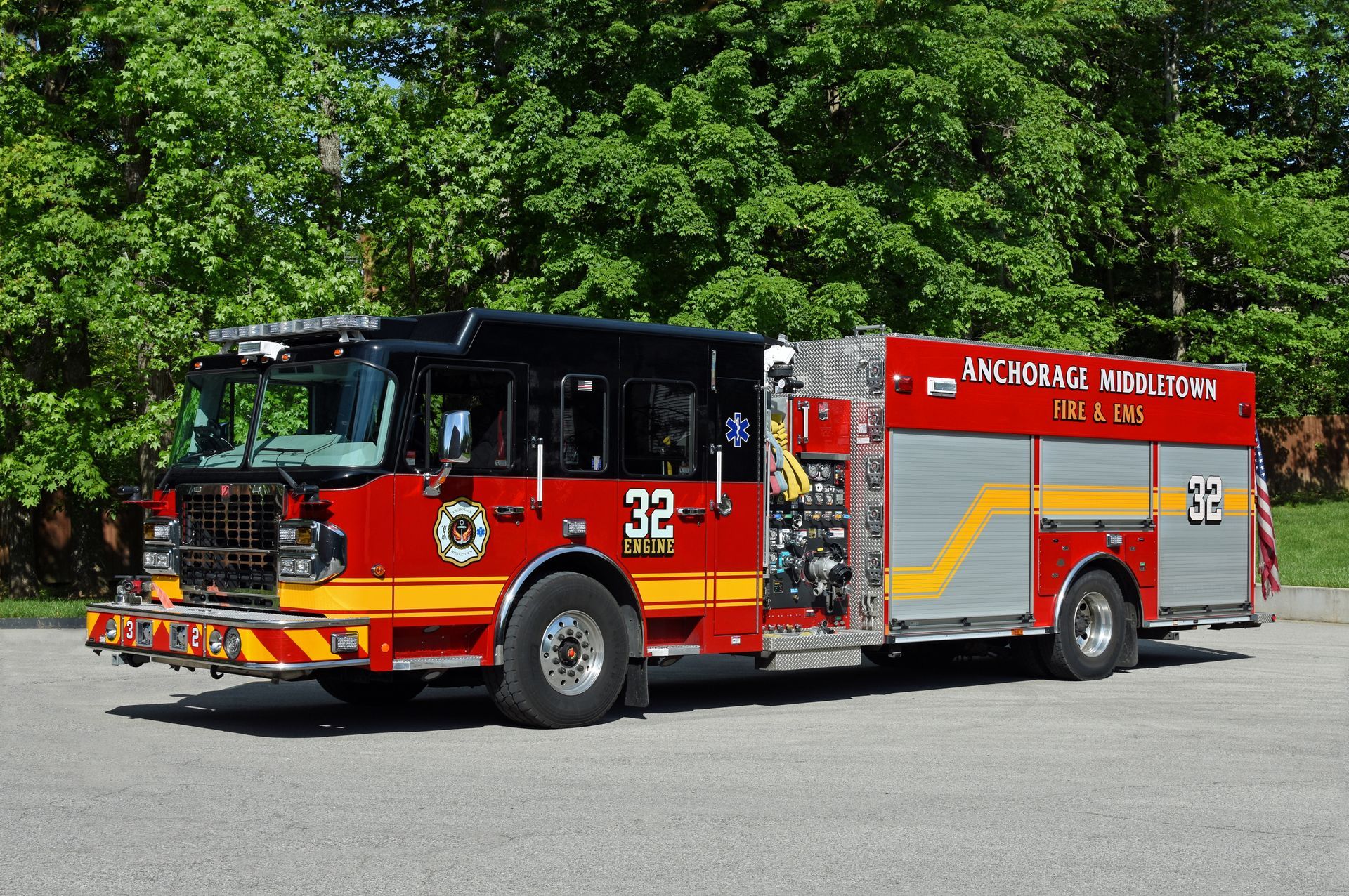 Red and silver fire truck, number 32, parked in front of trees.
