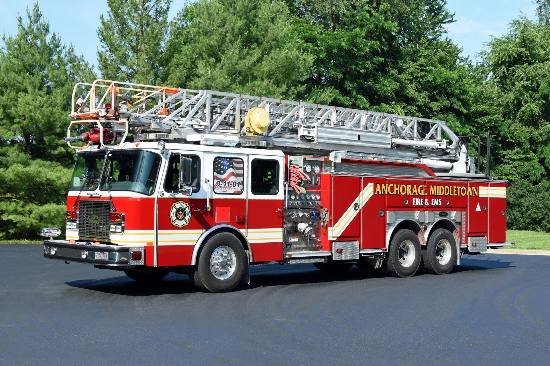 Red and white fire truck with a ladder, parked on asphalt with trees in the background.