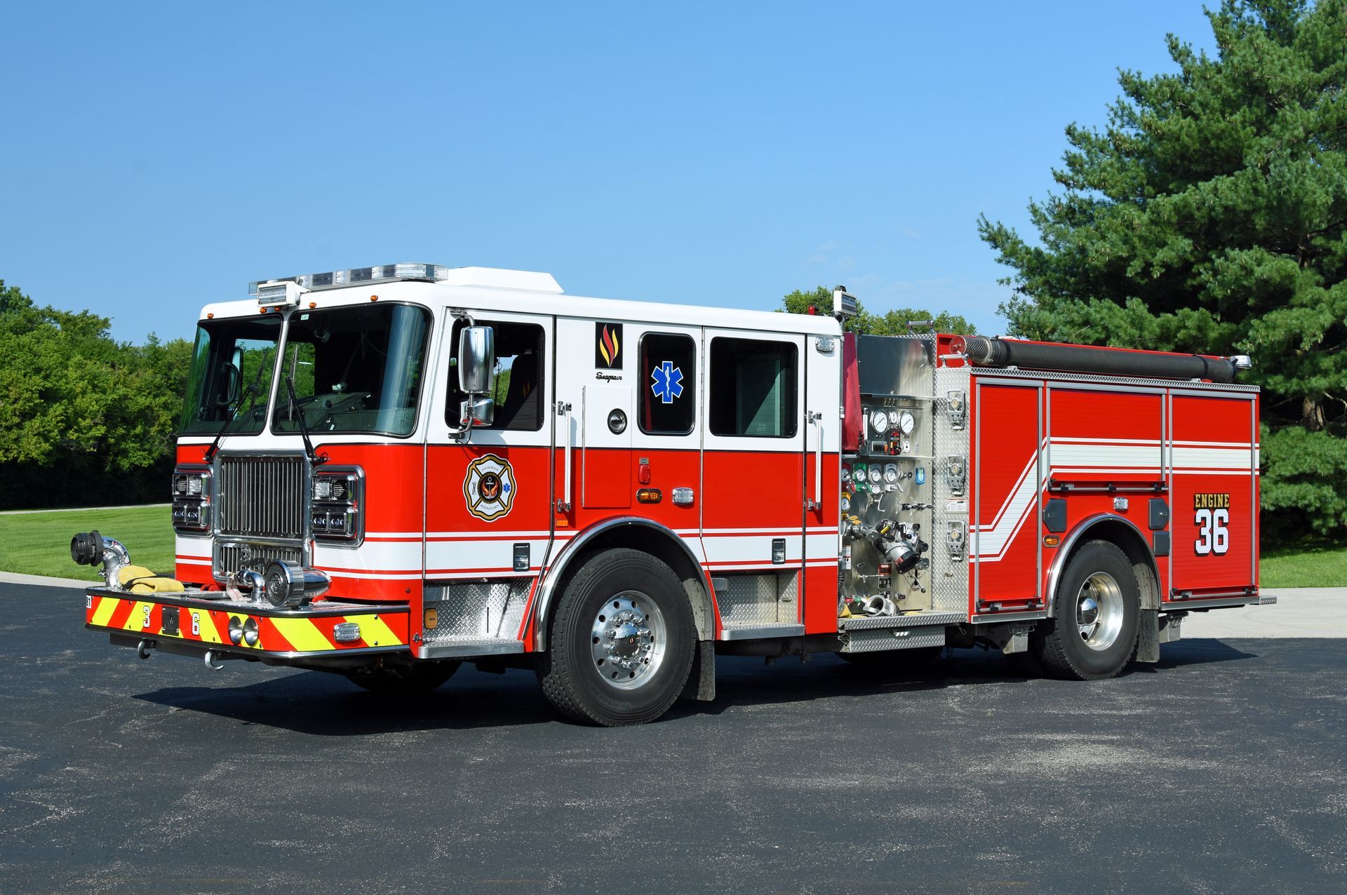 Red and white fire truck parked on asphalt, number 36 on side, with trees in the background.