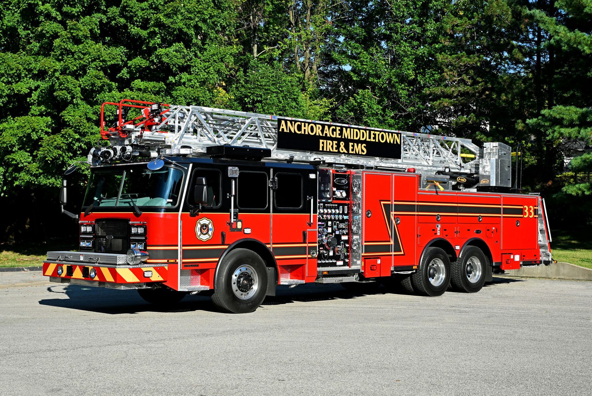 Red fire truck with extended ladder on a paved area, green trees in background.