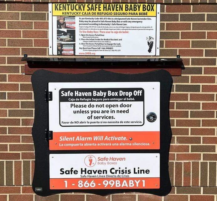 Kentucky Safe Haven baby box on a brick wall with hotline signs and emergency drop-off instructions