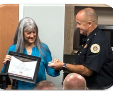 Woman in blue shirt receives award from uniformed man; indoor setting.