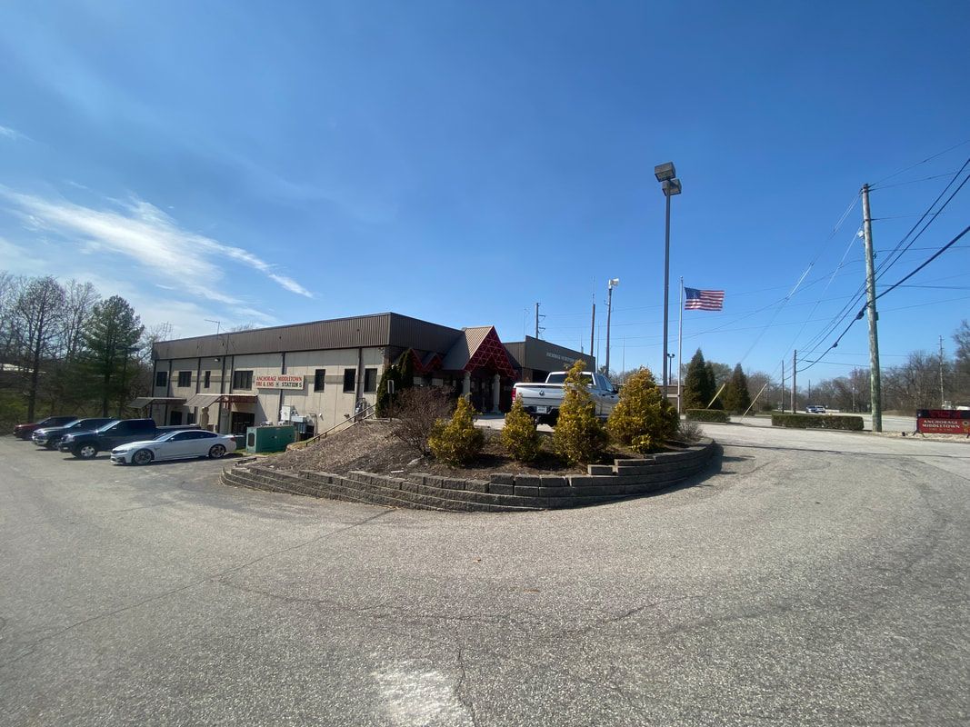 A building with a sign, parking lot, American flag, and clear blue sky.