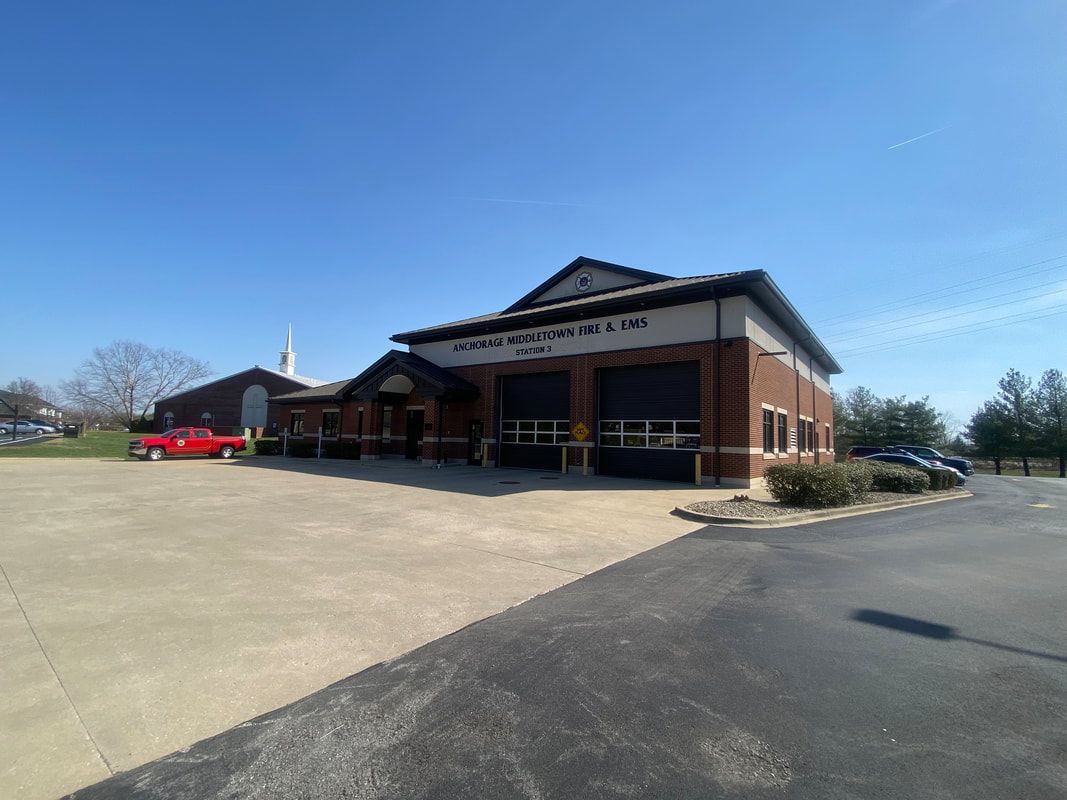 A two-story brick building with a dark roof and a paved parking lot. A red truck is parked in front of the building.