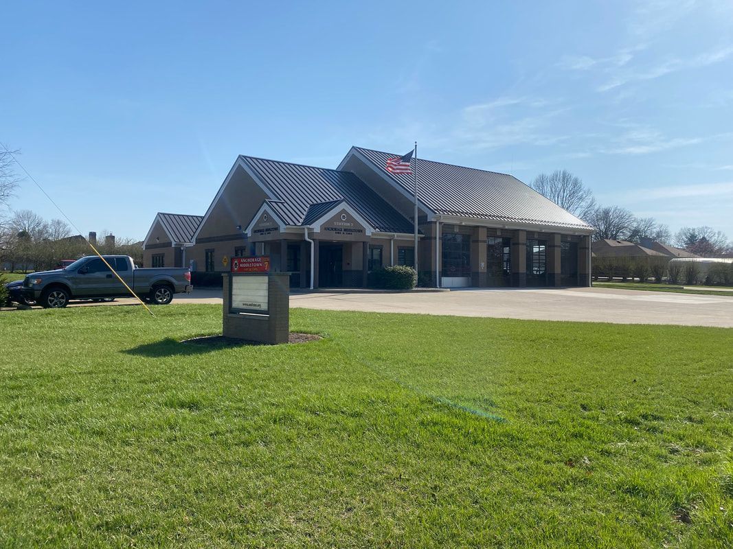 Building with black roof and awning, green lawn, clear blue sky, pickup truck parked nearby.