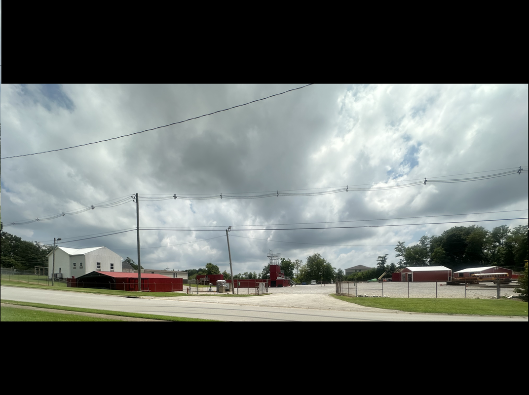 A rural scene with a parking lot in front of red buildings and a white building under a cloudy sky.