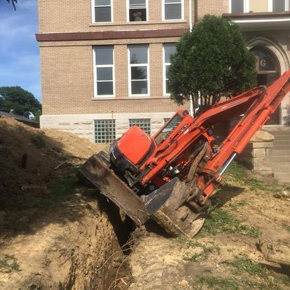 sewer line repair dayton oh An orange excavator digging a trench in front of a brick building with windows.