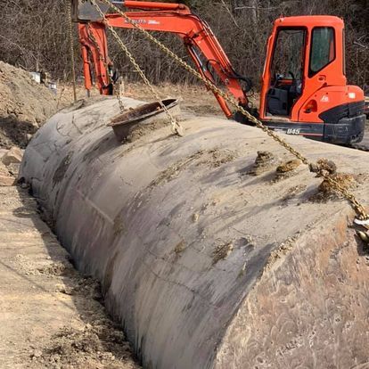 sewer line repair dayton oh An excavator lifts a large, buried metal tank from a trench.