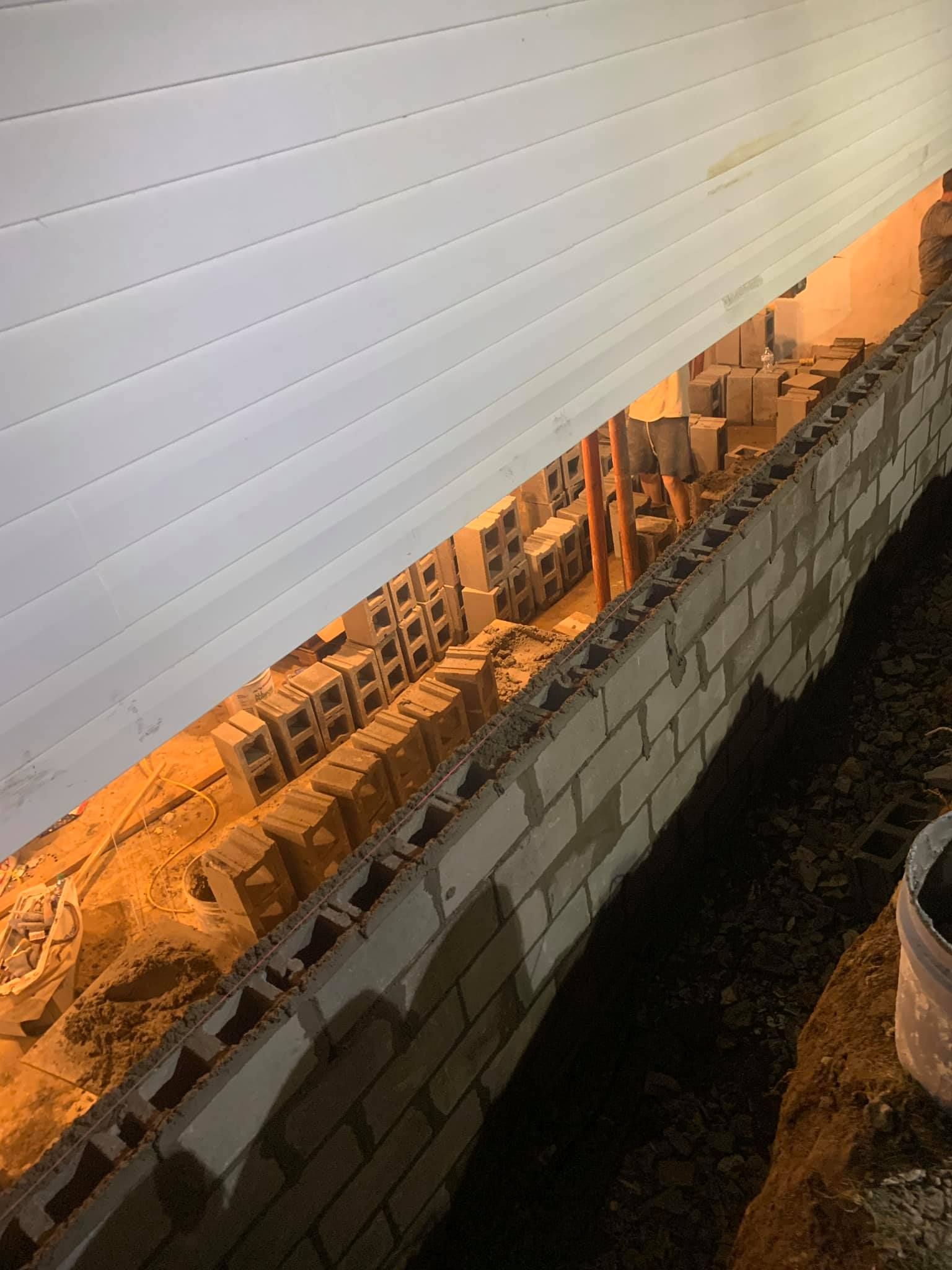 foundation repair dayton oh Damaged brick wall with a view of buildings beyond, under a corrugated white roof.