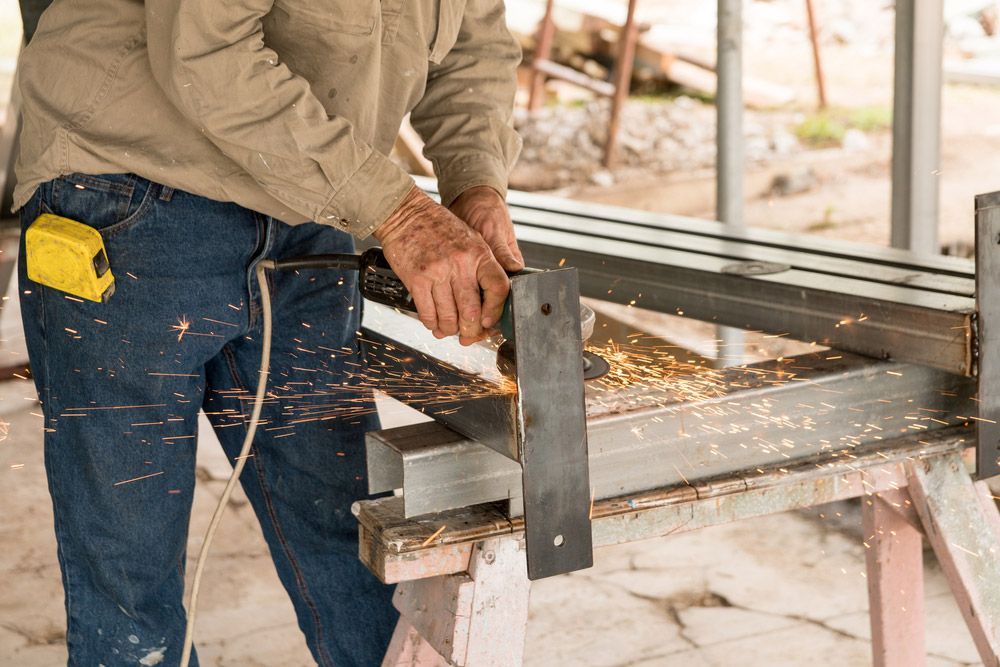 A Man Is Cutting a Piece of Metal with A Grinder — Magnum Steel In Crestwood, NSW