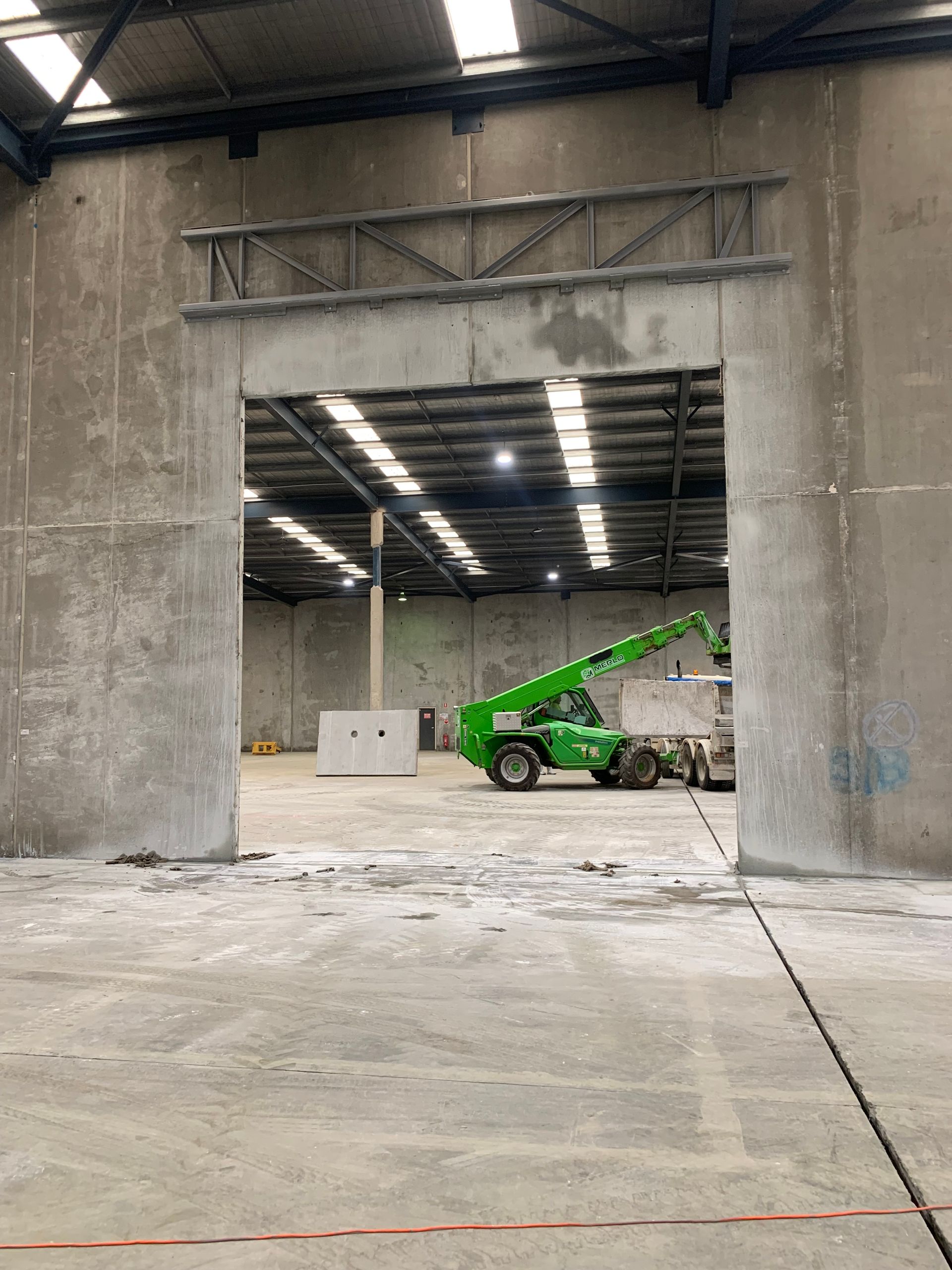 A green forklift is driving through a doorway in a warehouse — Magnum Steel In Crestwood, NSW
