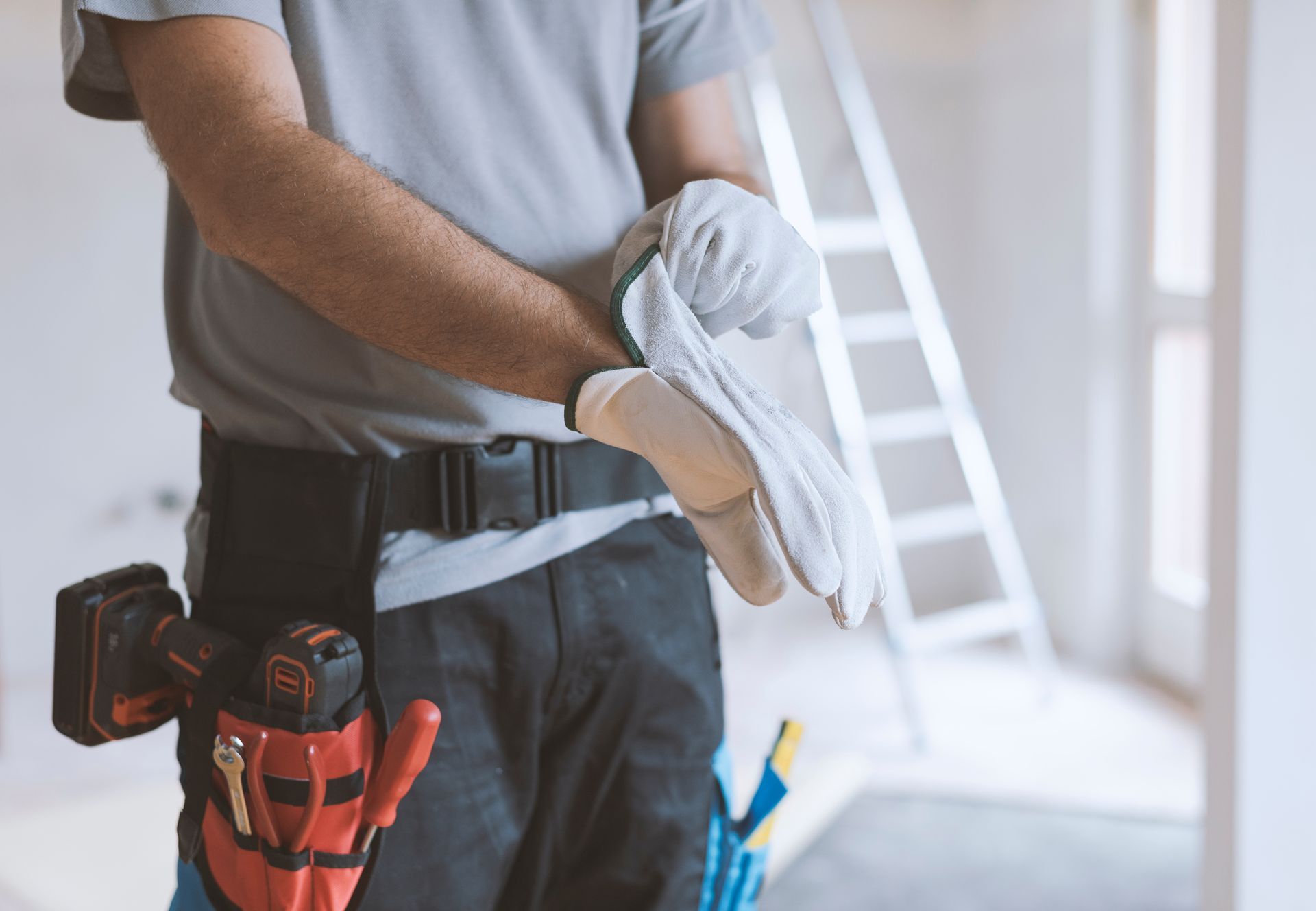 Worker holding folded white cloths at a construction site, with tools in a belt and a ladder in the background Worker holding folded white cloths at a construction site, with tools in a belt and a ladder in the background