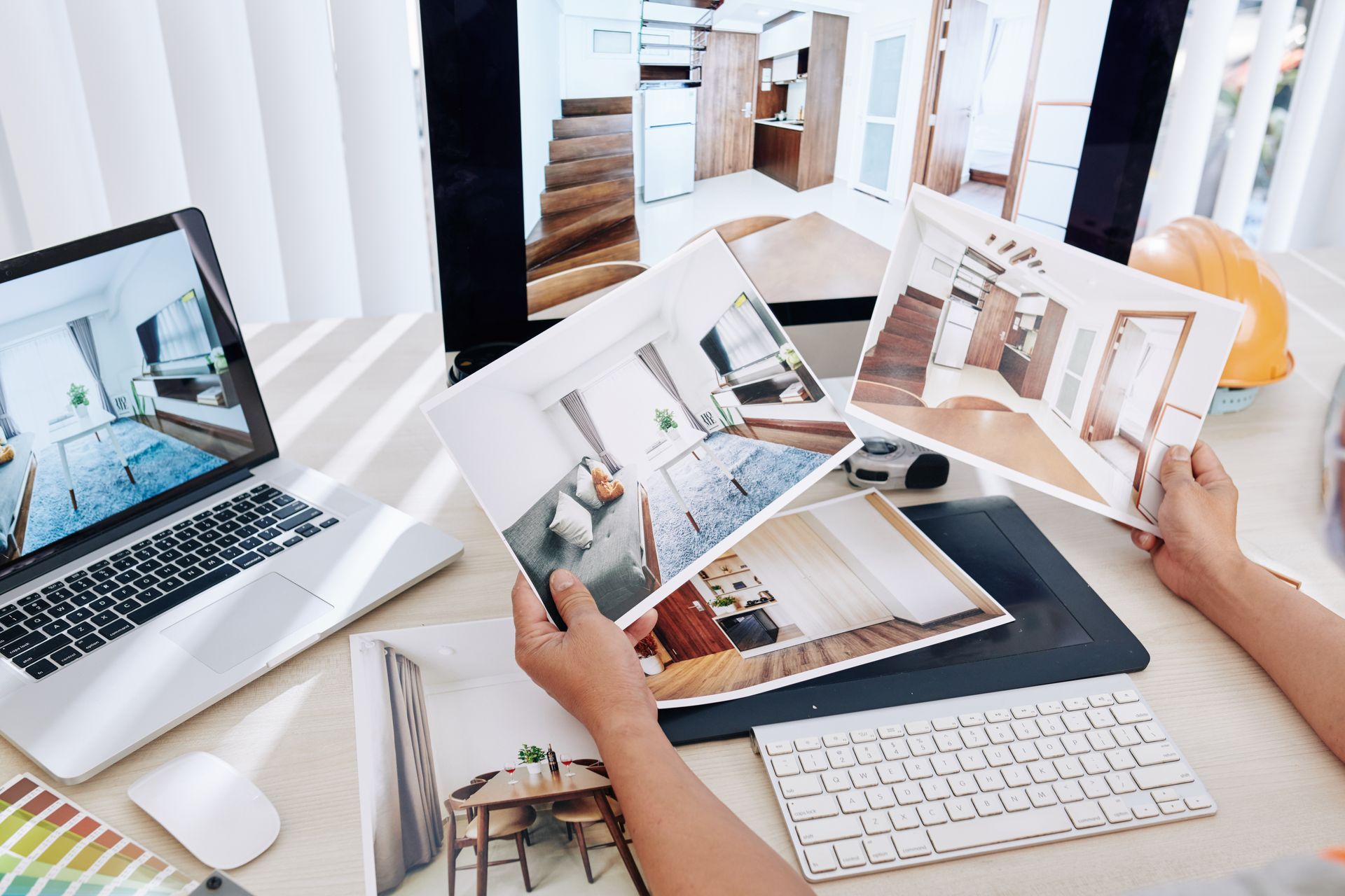 Two people reviewing interior design photos at a white desk with laptops and printed room layouts Two people reviewing interior design photos at a white desk with laptops and printed room layouts