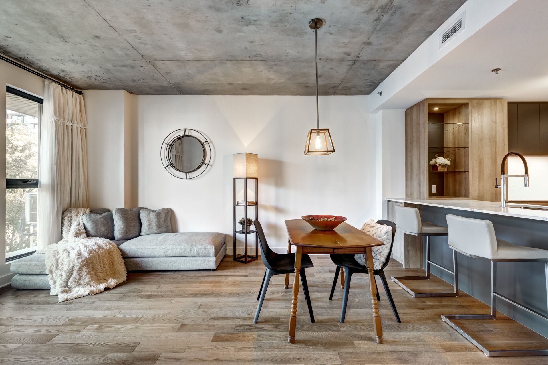 Modern open-plan living room with gray sofa, round dining table, and kitchen bar in a bright neutral interior Modern open-plan living room with gray sofa, round dining table, and kitchen bar in a bright neutral interior