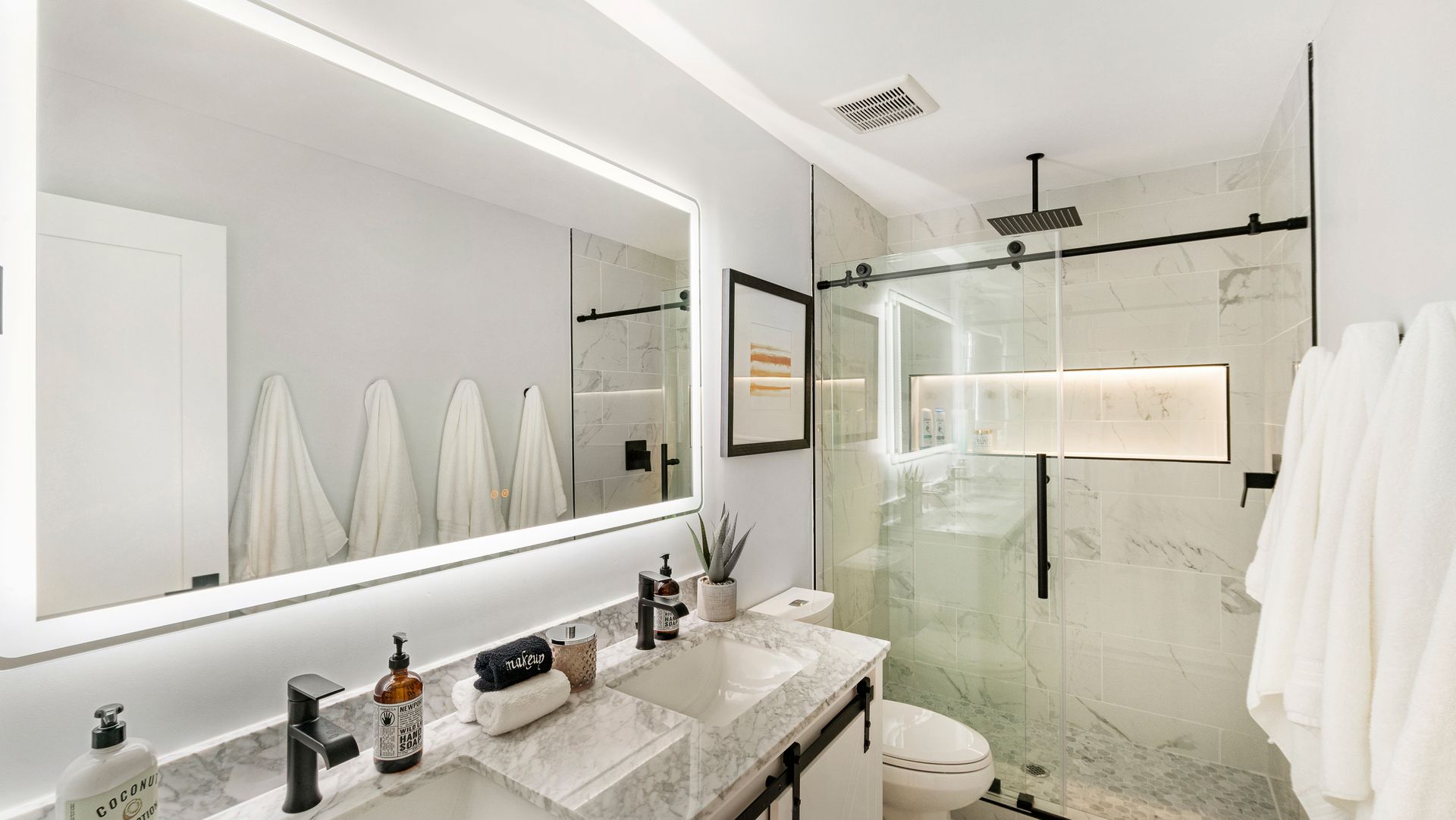 Bright modern bathroom with large mirror, double sink, glass shower, and white towels hanging on the wall. Bright modern bathroom with large mirror, double sink, glass shower, and white towels hanging on the wall.