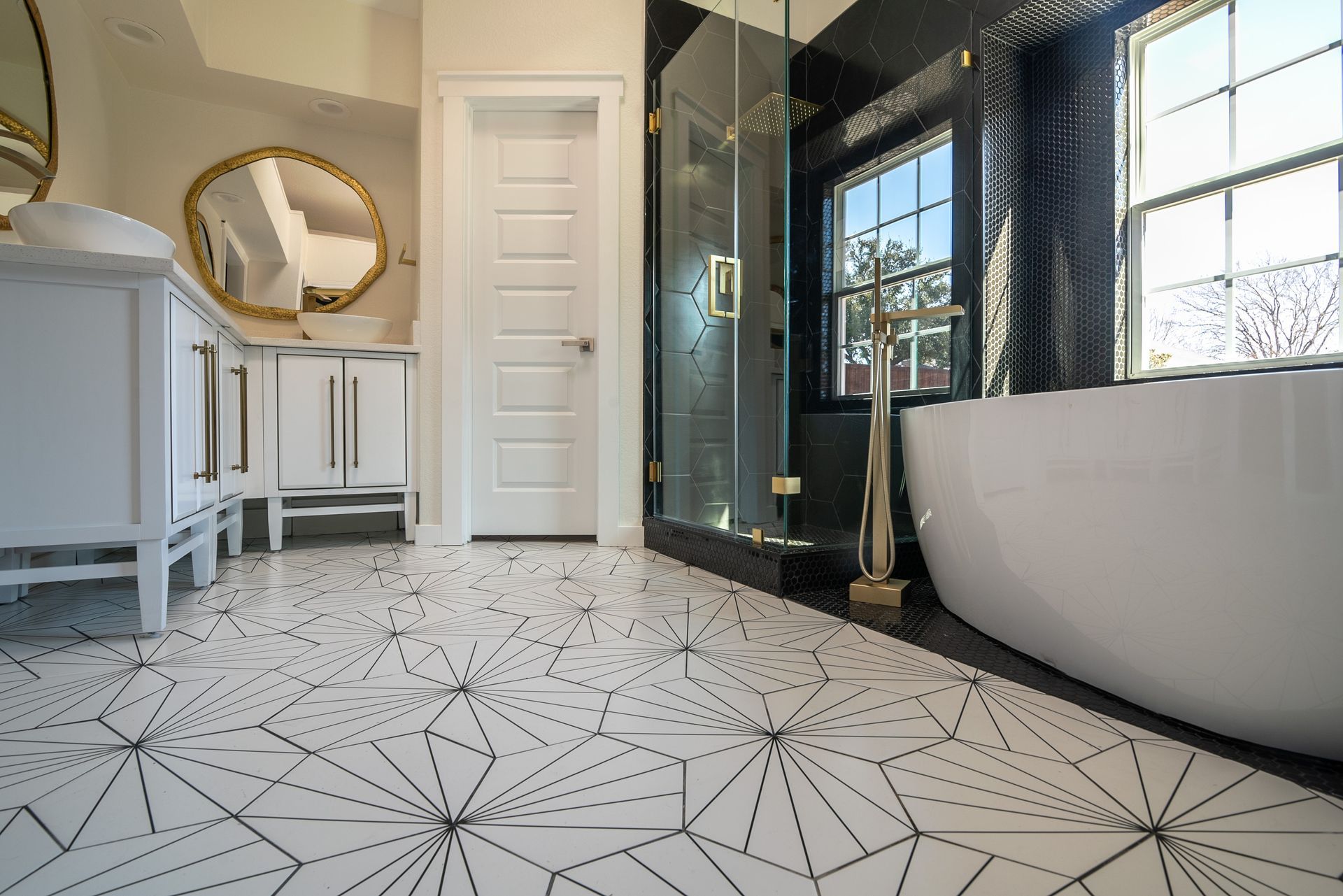 Bright bathroom with freestanding tub, glass shower, white vanity, and geometric black-and-white floor tiles.